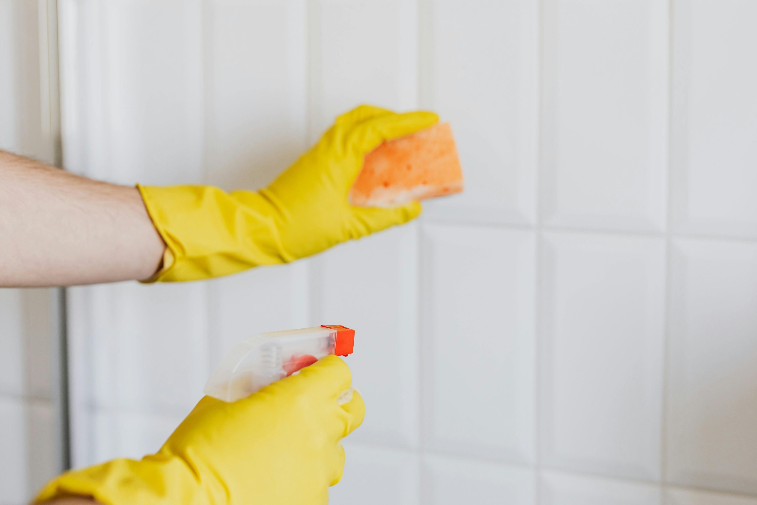 close-up of hands in yellow rubber gloves, cleaning bathroom tiles with a sponge